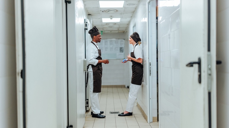 Two chefs wearing white and black aprons enjoying a break, engaged in a conversation about the 10 best non-slip shoes for restaurant workers.