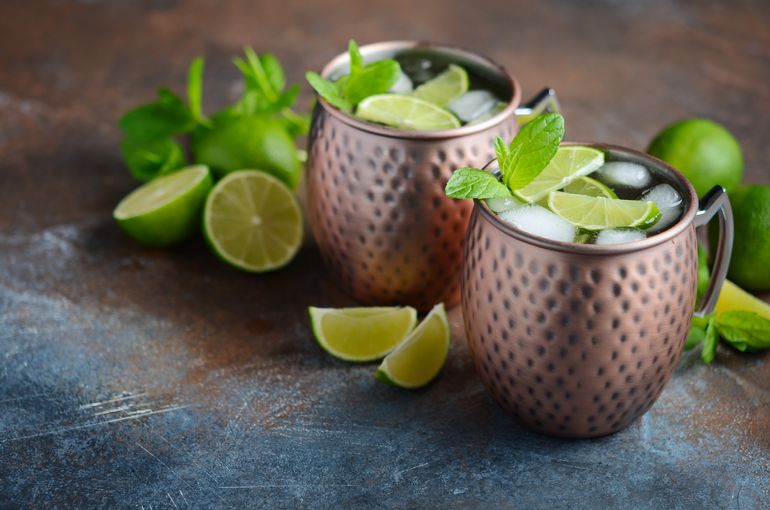 Two Wells drinks with green garnishes and lime surrounded by more limes.