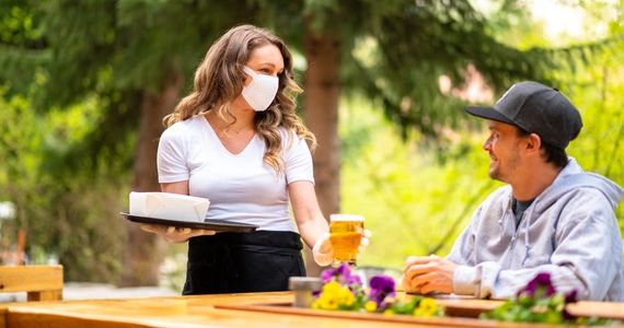 Server wearing a face mask handing a man a beer on an outdoor patio