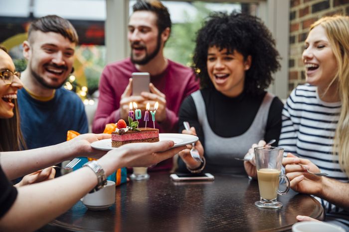 Server delivering a slice of birthday cake to a table of friends