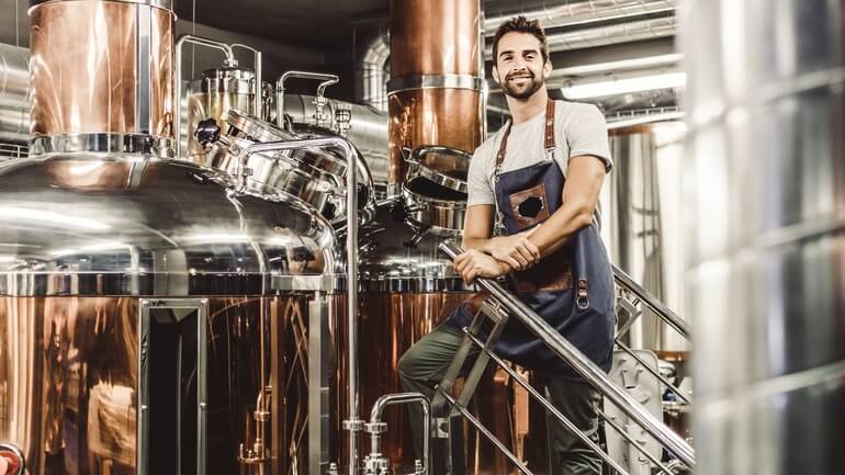 A worker standing next to commercial brewery equipment. 