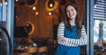 Image of woman restaurant owner opening the front door to her restaurant and smiling, thinking of creative names for restaurants.