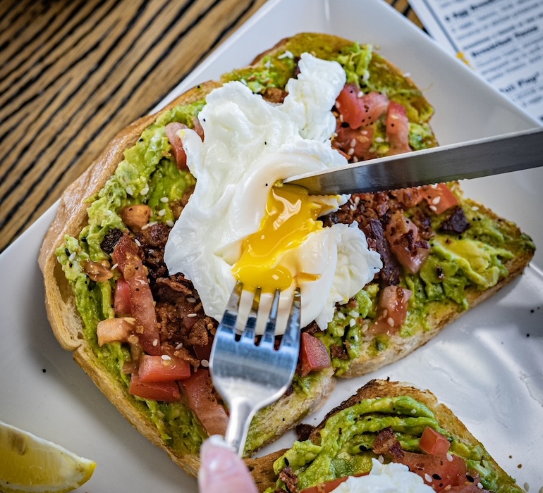 Avocado toast with a runny egg on top being cut into.