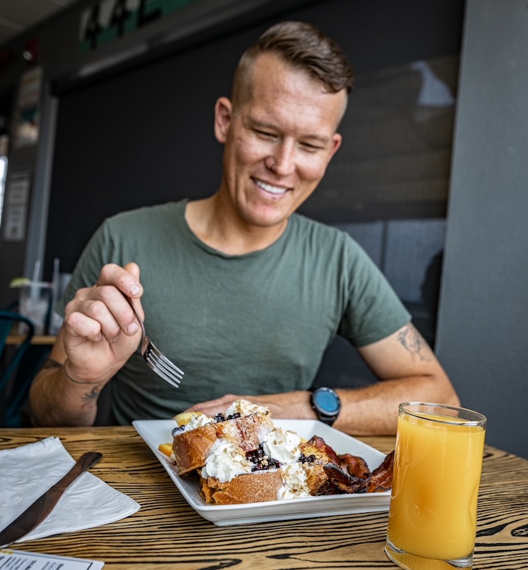 A person sitting at a restaurant table eating their breakfast with a glass of orange juice.