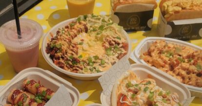 Smoothies, poutine, rice bowl, bao buns, and egg sandwiches displayed on a yellow tablecloth outside.