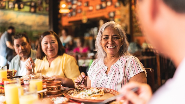 A group of 4 seniors at a restaurant enjoying a meal and conversation together. 