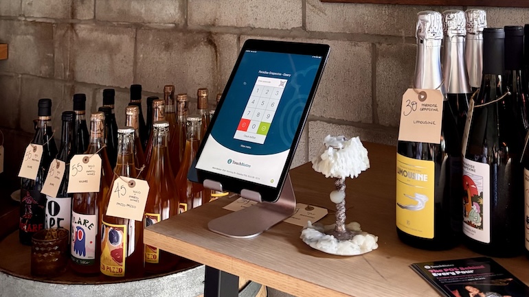 TouchBistro POS iPad on a stand on a table next to wine bottles.