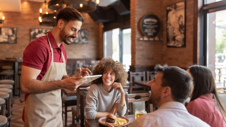 restaurant server taking a table of three's order using a tablet.